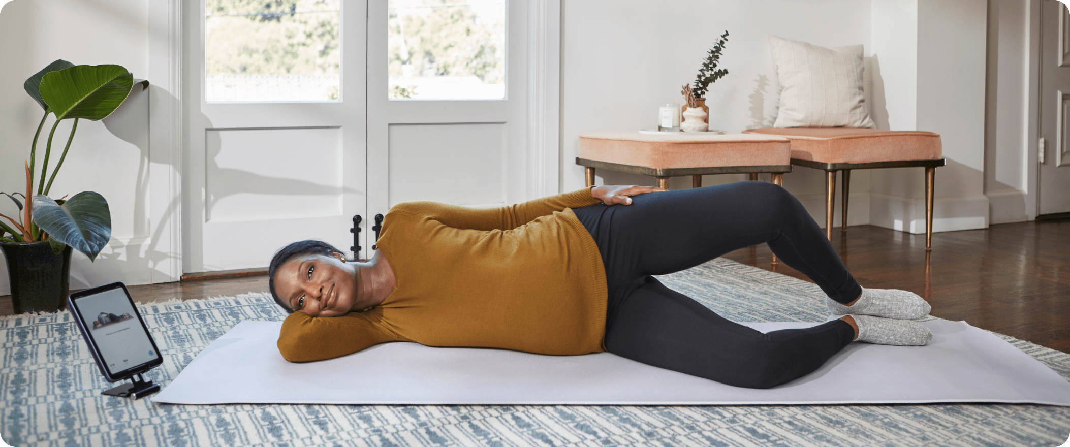 Woman laying on mat and doing exercises with Hinge Health tablet