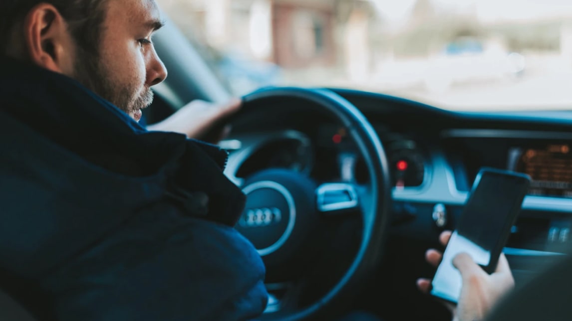 A distracted man looks at his phone while driving.