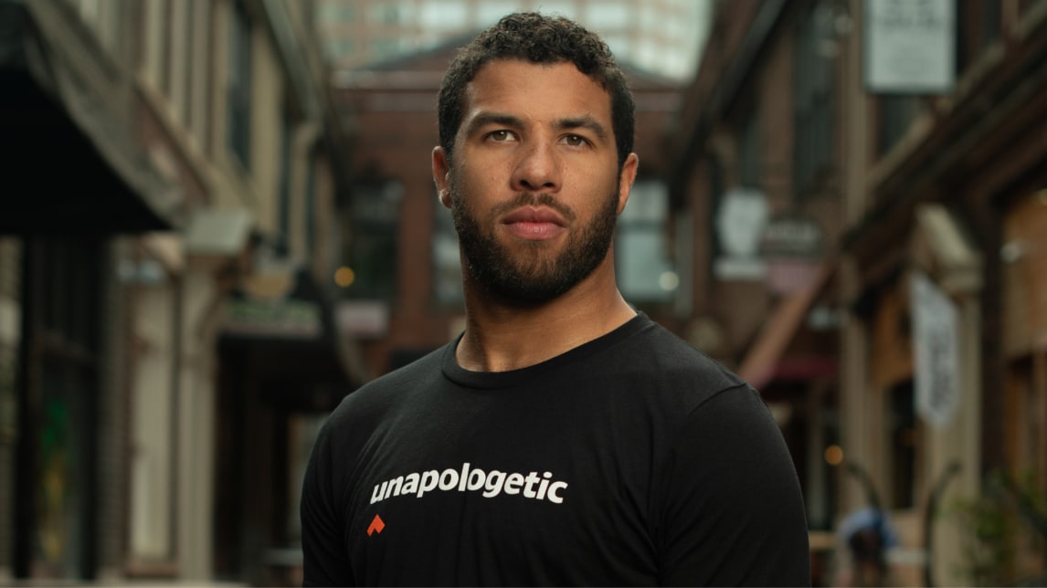 NASCAR driver Bubba Wallace stands in front of a blurred background.