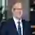 Anthony Alosi with glasses and a gray beard wearing a navy suit and blue tie in a professional headshot.