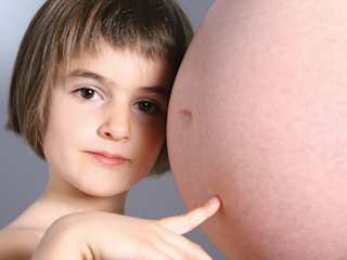 Kind berührt den Babybauch der Mutter