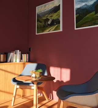 Ein Zimmer mir einer roten Wand, zwei Bildern, zwei Stülen und einem Tisch
