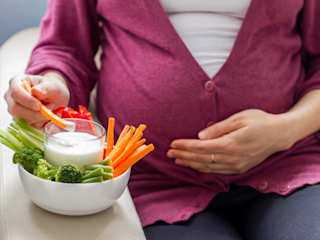 schwangere hält ihren Bauch und isst Gemüse