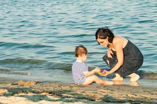 Mutter und Kleinkind spielen am Strand