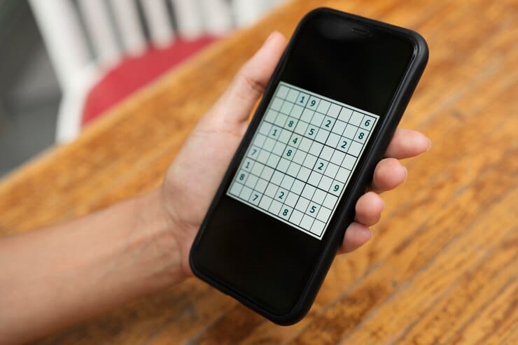 A person holding a smartphone over a brown table showing a puzzle game