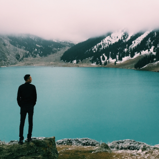 A person on a rock looking out at a senic body of water and mountains
