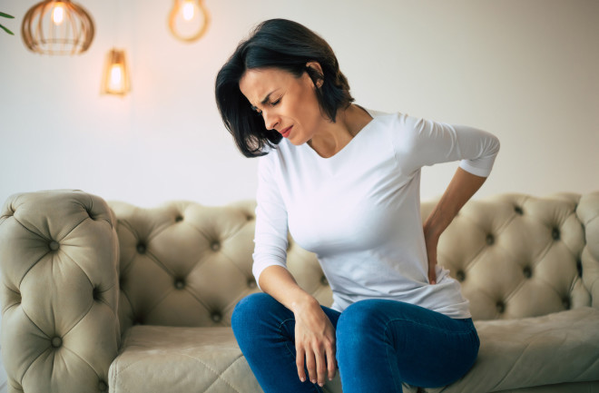 woman sitting on couch holding lower back from back pain