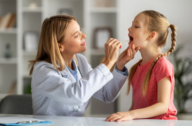 Female pediatrician checking throat of little girl patient with strep throat