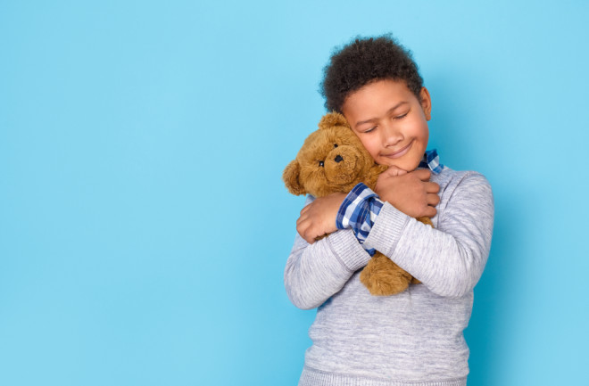 One boy studio isolated on blue wall hugging teddy bear tight