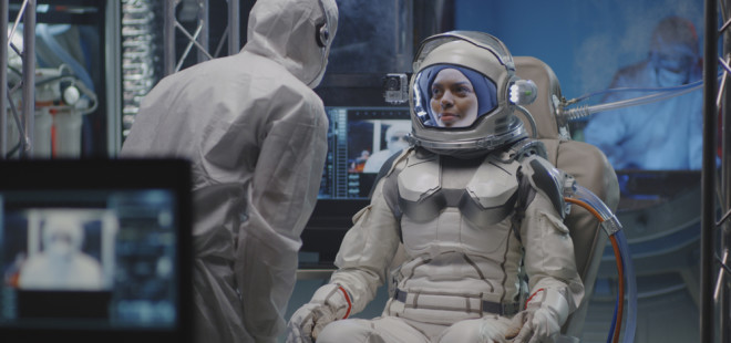 Medium shot of a female astronaut testing spacesuit camera and listening to instructions during pre-flight preparation