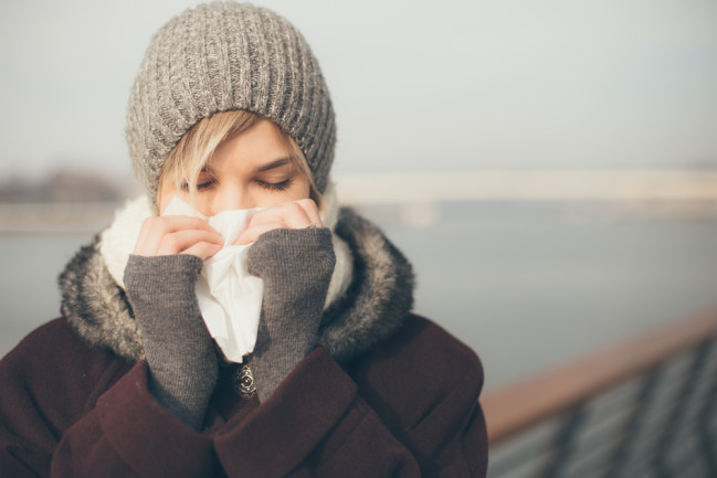 woman outdoors blowing her nose and sick from the cold