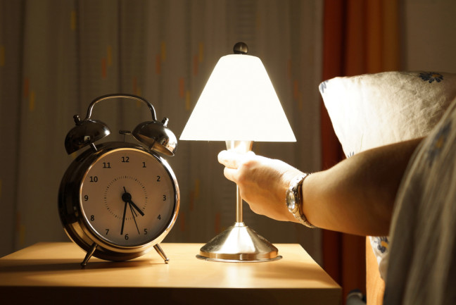 Arm reaches out of bed and turns on a light in the middle of the night - Shutterstock