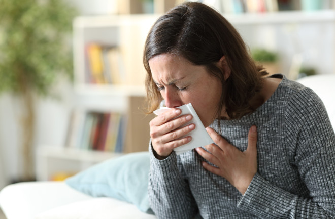 woman coughing phlegm into a tissue at home