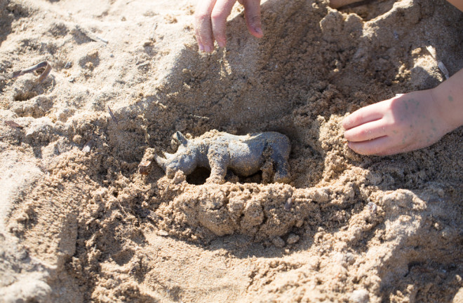 Child Playing with Rhino Toy Figurine in Sand at a Beach - Shutterstock