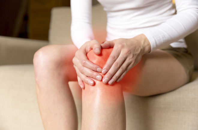 Woman holding her inflamed knee, inflammation - Shutterstock