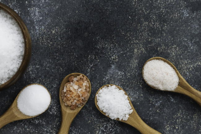 Various salt types in 4 wooden spoons on dark background.