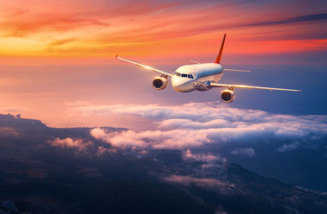 Passenger airplane. Landscape with big white airplane is flying in the sky over the clouds and sea at colorful sunset.