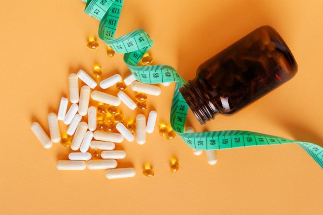 Weight Loss Pills Scattered from Bottle on Yellow Background