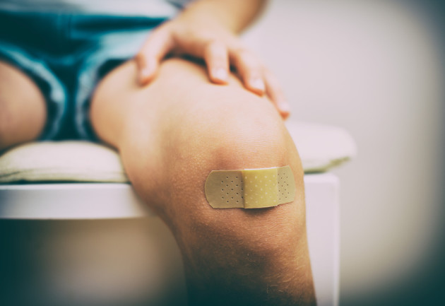 child sitting down with a bandaid on knee - shutterstock 212590312
