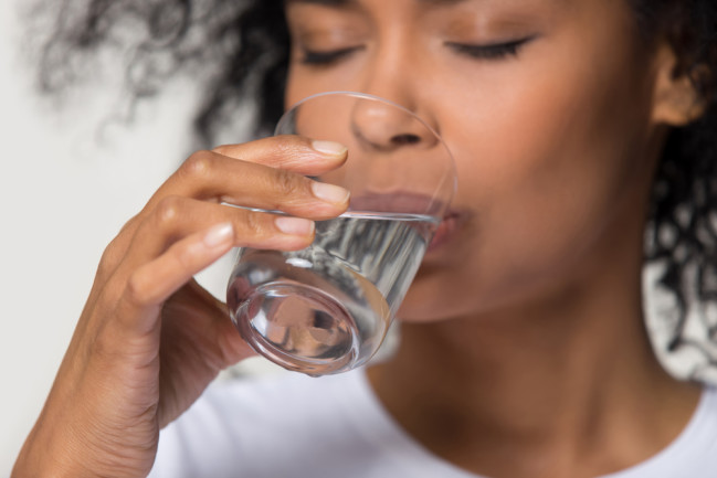 close up of woman drinking a glass of water - shutterstock 1391203490