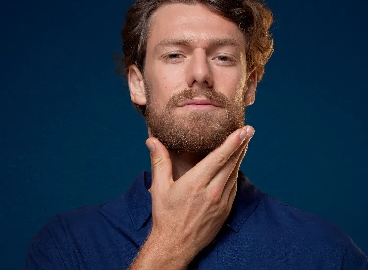 Person wearing gray sweater touching jawline against dark blue background