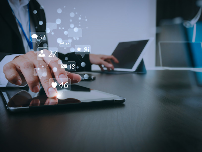 Male real estate broker typing on two different tablets with social media icons floating in the air with numbers of likes and emails.