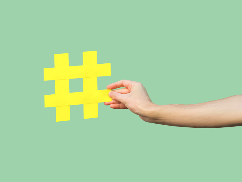 Close-up of hand holding large yellow hashtag sign