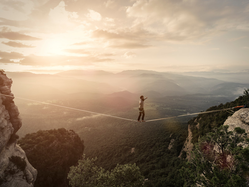 Man walking tightrope across ravine at dawn