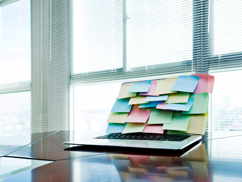 Laptop computer with screen covered in multicolored sticky notes.