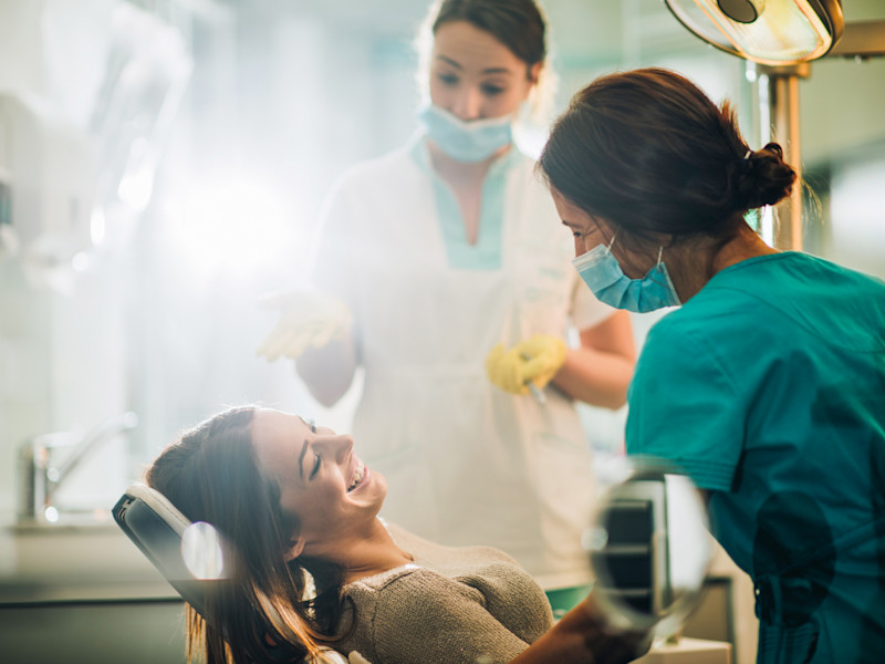 Smiling woman sitting in dentist chair and talking to her dentist before teeth examination.