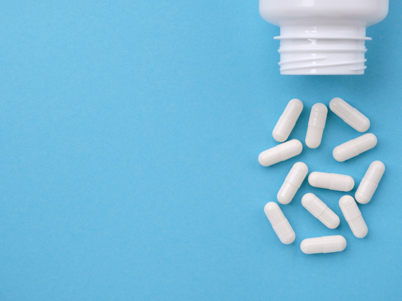 White medication bottle spills 12 white capsules on a light blue background.