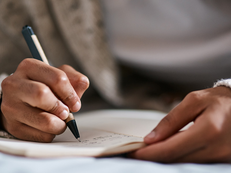 Woman in a beige sweater writing a draft of her cover letter in her notebook.