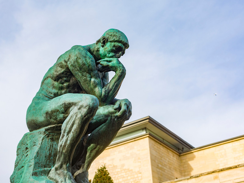 Augustin Rodin's famous sculpture The Thinker against the backdrop of a sunny day and blue sky.