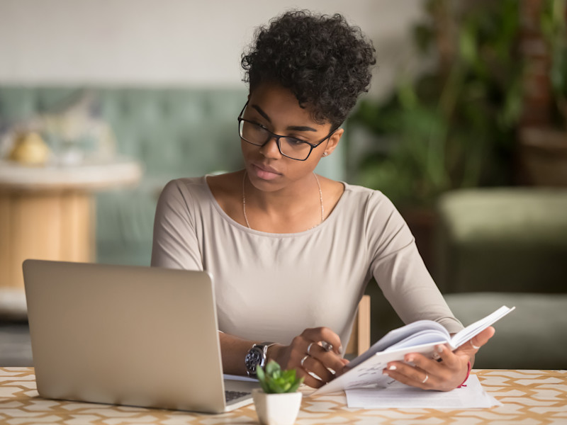 Young African American woman with glasses reading article on computer and taking notes