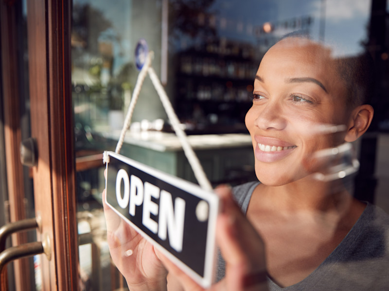 Young business woman of color hanging an Open sign in her store's window.
