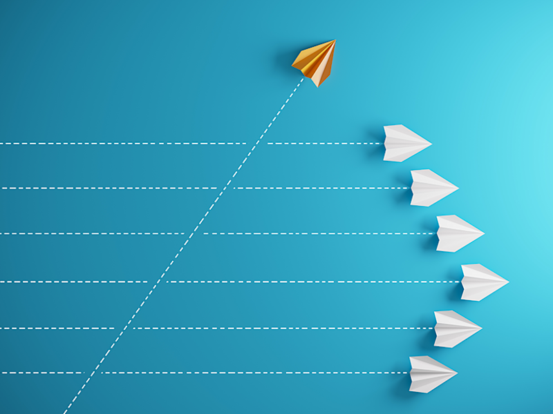 White paper airplanes flying in one direction and an orange plane flying in a different direction