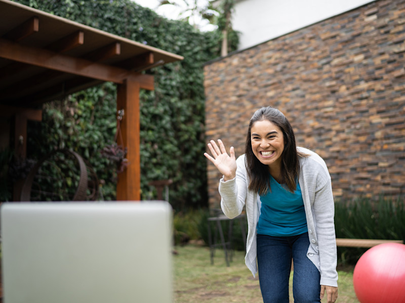 Woman teaching exercise online waving to webcam at home