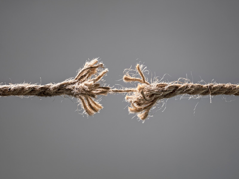 Two pieces of frayed rope connected by a single thread