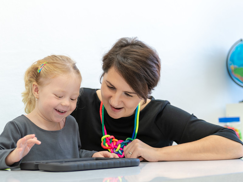 Female toddler in occupational therapy session doing playful exercises on a digital tablet with her occupational therapist.