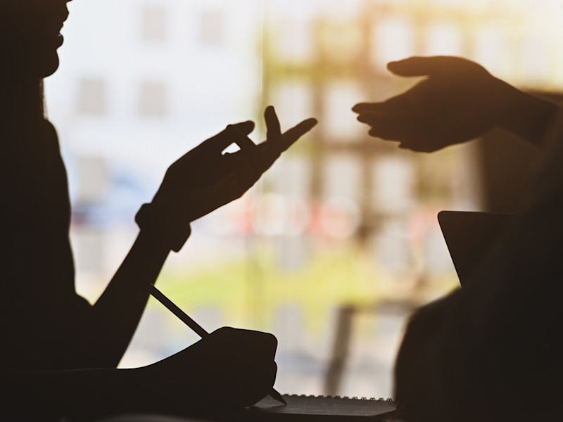 Silhouette of two people chatting and networking while one of them writes things down.