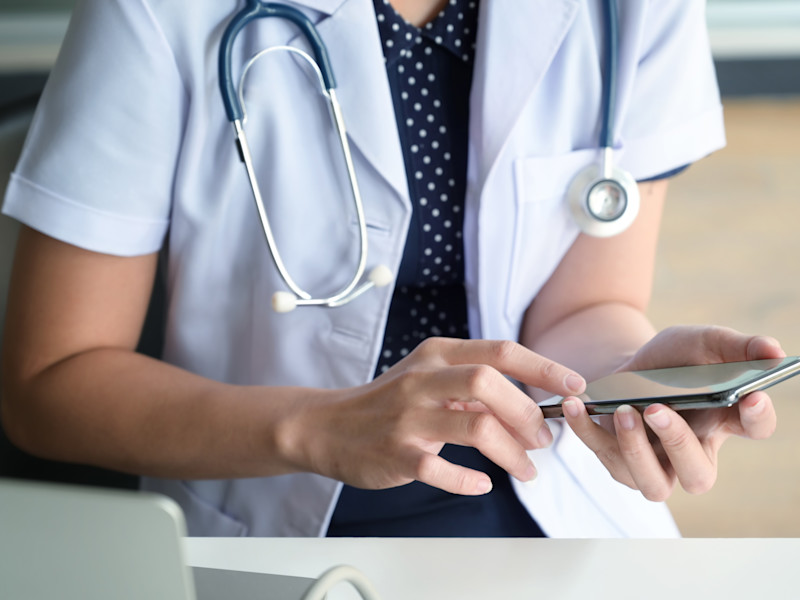 Female nurse with stethoscope around neck using her smartphone to look up medical information.