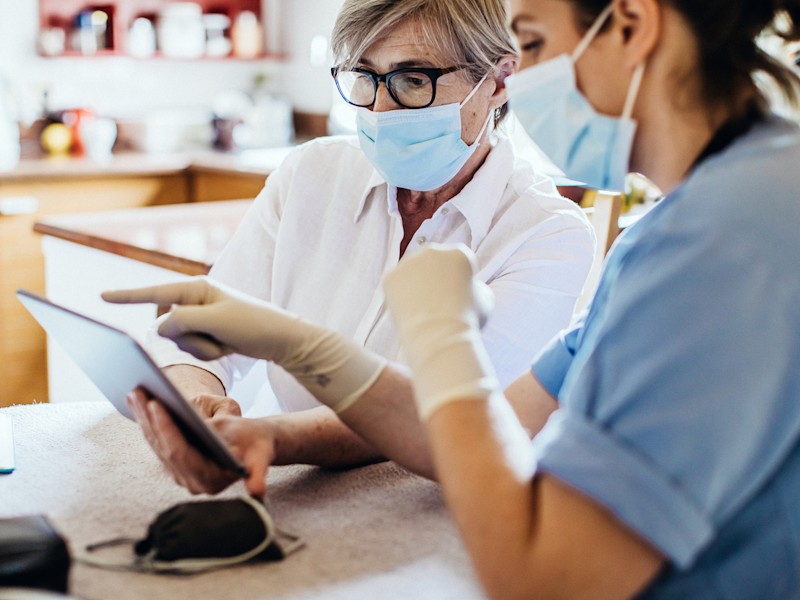Masked nurse showing a masked female patient information on an ipad