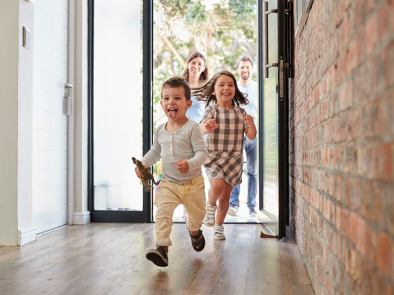 Children running into open house with parents behind them