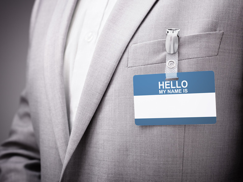 Male torso in a light gray suit wearing a blank "Hello my name is" nametag.