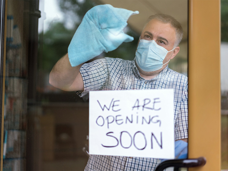 Man in face mask wiping door with open for business sign
