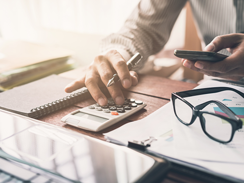 Male real estate agent sitting at his desk typing on a calculator while reviewing business documents.