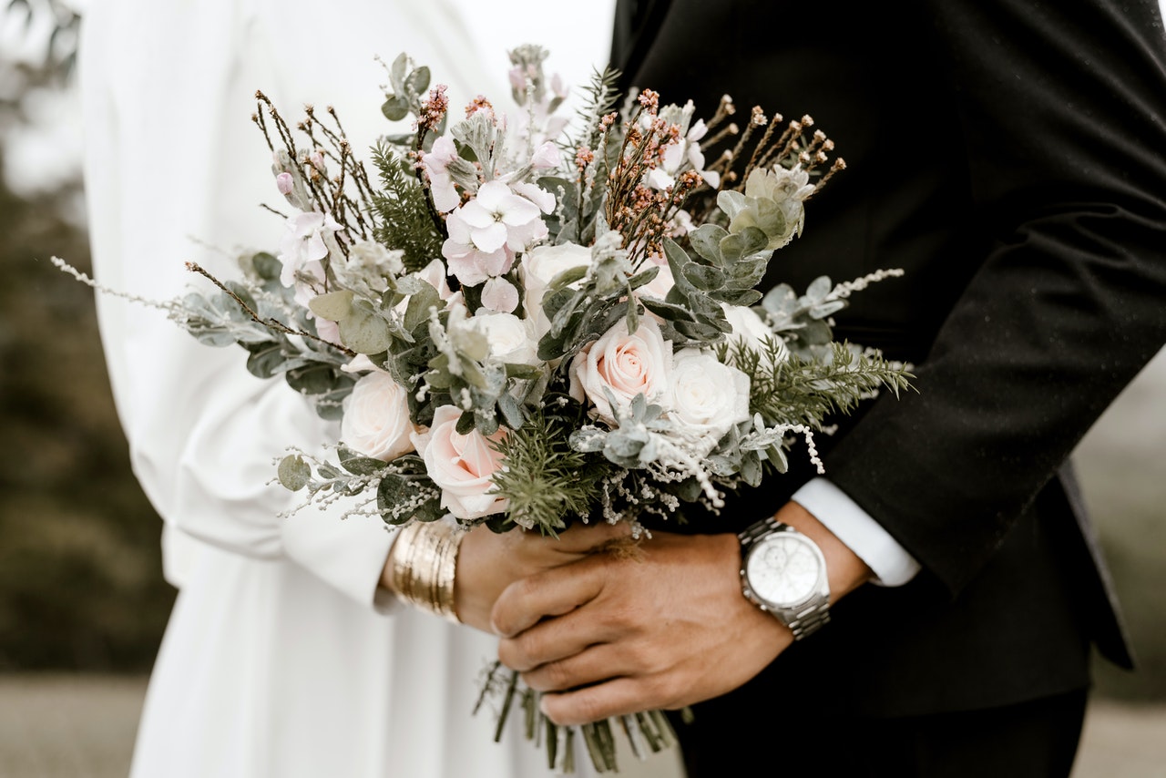 Bride and groom standing next to each other holding hands with a bouquet 