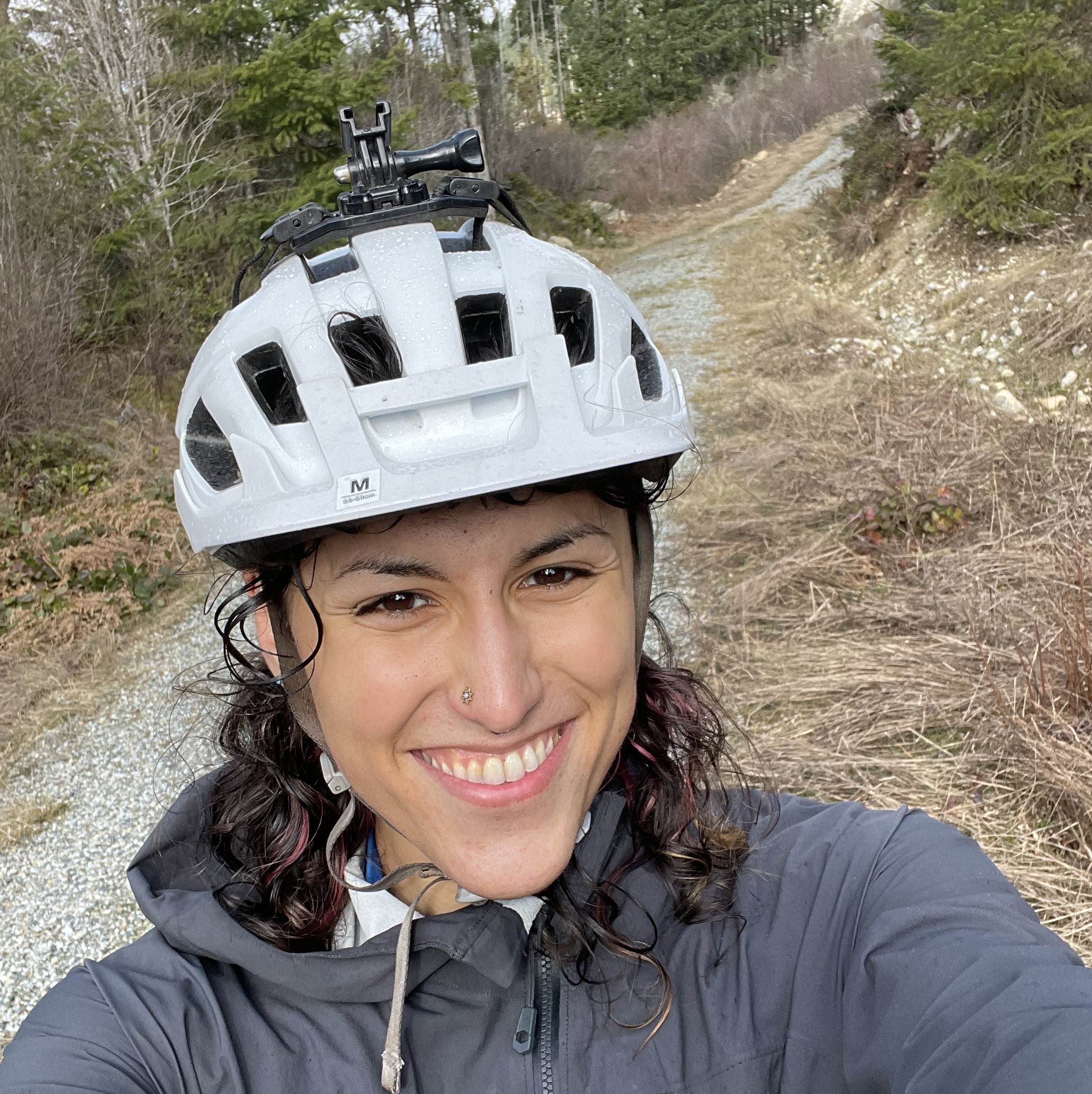 An image of Noah smiling and wearing a white bike helmet, against the background of a gravel trail in the fall.