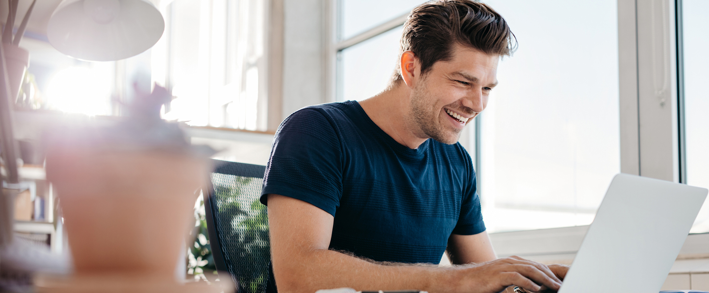 Een man zit in het thuiskantoor aan zijn bureau naast een groot raam