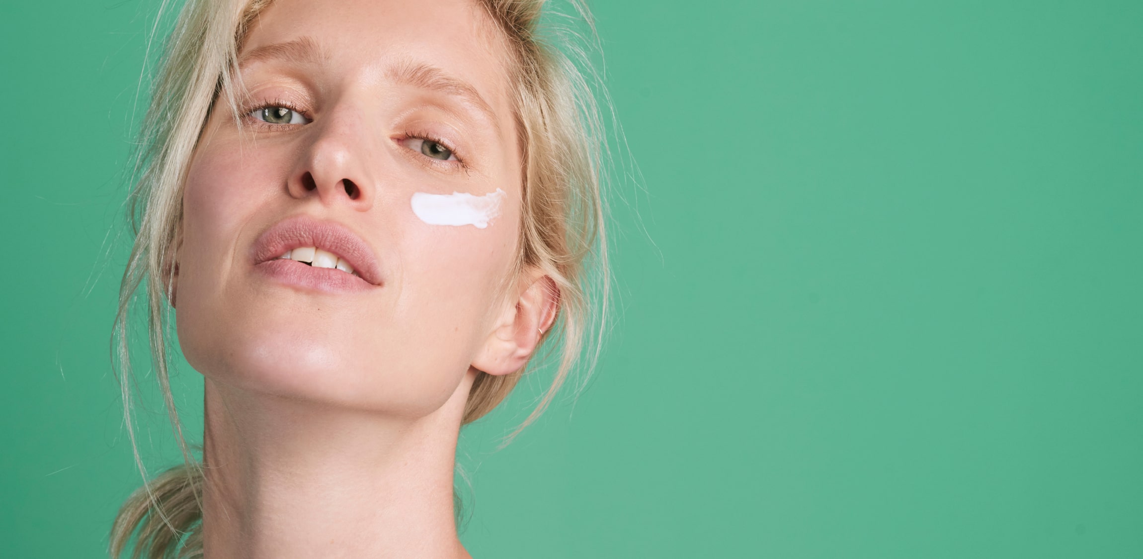 Een vrouw heeft een streepje zalf op haar huid gesmeerd en staat voor een groene achtergrond